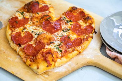 心形的意大利辣香肠披萨放在披萨皮上，然后是一堆盘子